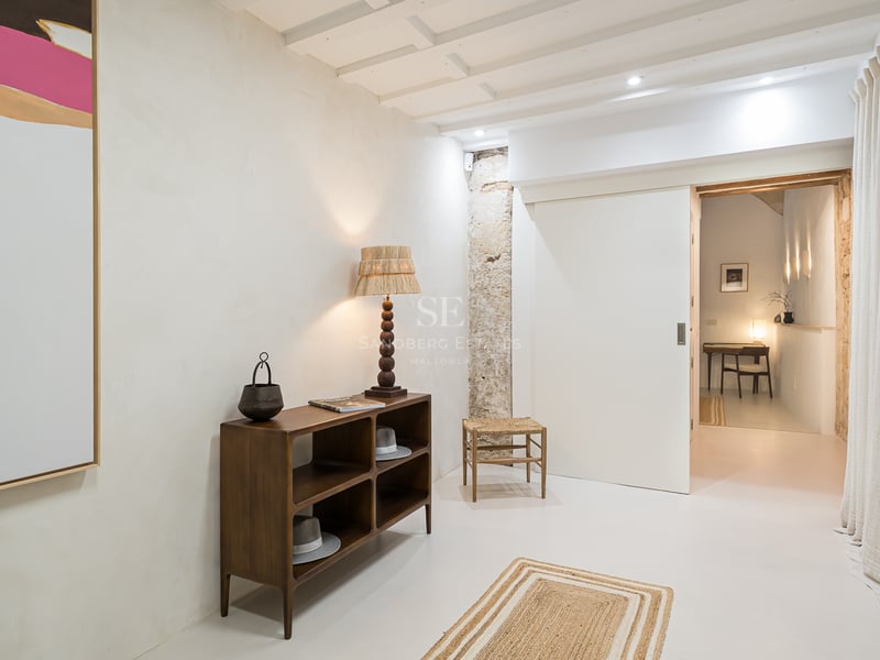 Couloir moderne avec murs en plâtre blanc, console en bois, lampe rustique et vue sur un bureau.