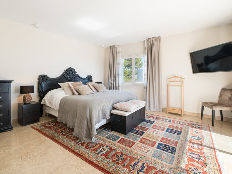 Chambre principale lumineuse avec tête de lit noire ornée, tapis à motifs et sol en travertin.