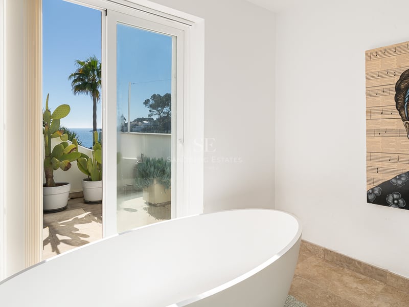Salle de bain moderne avec baignoire blanche, portrait de Frida Kahlo et terrasse avec vue sur la mer.