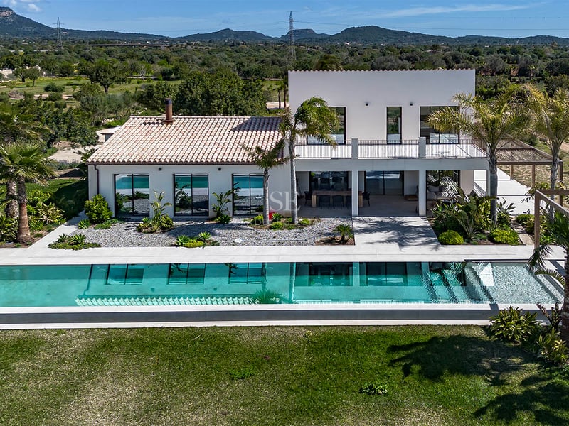 Vue aérienne d'une villa blanche moderne avec une piscine turquoise et un paysage de montagnes en arrière-plan.