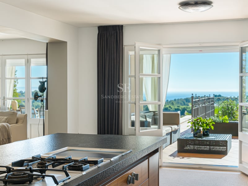 Îlot de cuisine moderne avec plan de travail en pierre noire, ouvert sur une terrasse ensoleillée avec vue sur la mer.