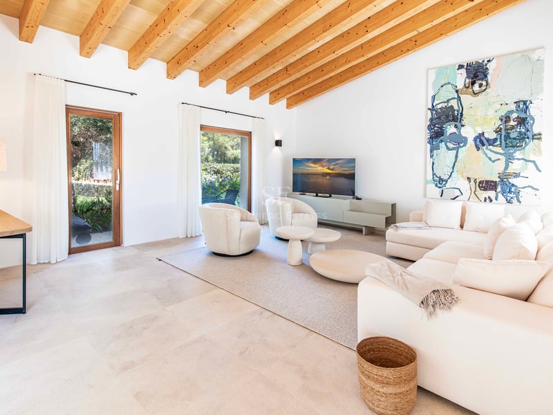 Salon moderne avec haut plafond à poutres, canapés blancs, sol en pierre naturelle et accès au jardin.