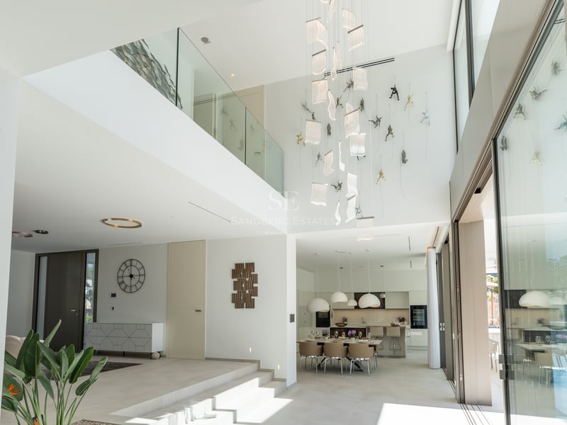 Espace de vie lumineux à double hauteur avec garde-corps en verre, luminaires design et baies vitrées.