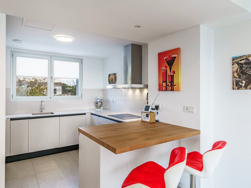 Cuisine moderne lumineuse avec placards blancs, bar en bois, tabourets rouges et électroménager en inox.