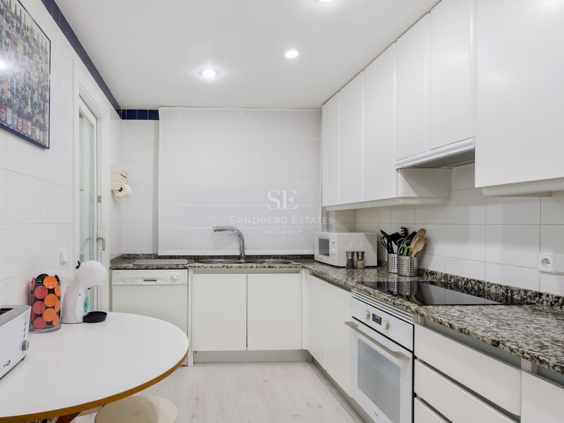 Cuisine moderne blanche avec plans de travail en granit, appareils intégrés et un petit coin petit-déjeuner.