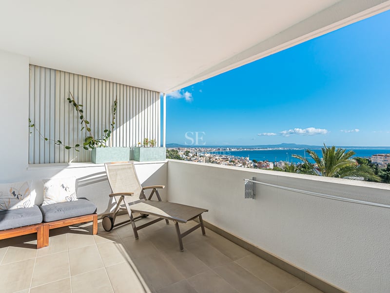 Grand balcon avec rambarde en verre, vue panoramique sur la mer et mobilier moderne de détente. Les plantes ajoutent une touche naturelle.
