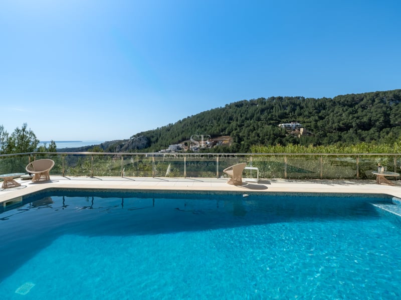 Piscine rectangulaire avec terrasse en pierre claire, garde-corps en verre et vue sur des collines verdoyantes.