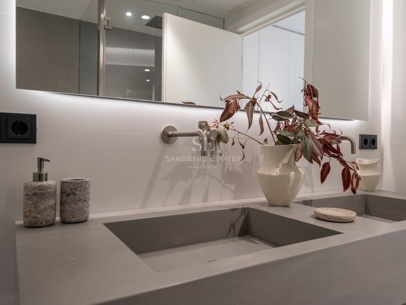 Double vasque grise intégrée avec robinetterie murale et miroir rétroéclairé dans une salle de bain moderne.