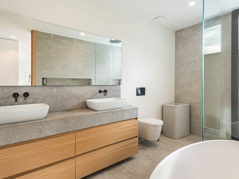 Salle de bain de luxe avec deux vasques sur un plan en pierre, meubles en bois et grand miroir.
