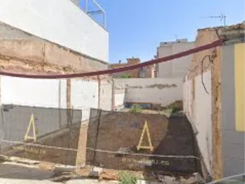 Vue d'un terrain à bâtir avec clôtures de chantier et murs de soutènement blancs.