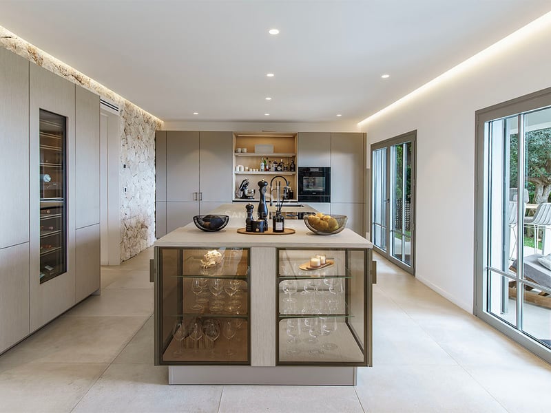 Cuisine contemporaine spacieuse avec îlot, cave à vin intégrée, mur en pierre naturelle et baies vitrées sur le jardin.