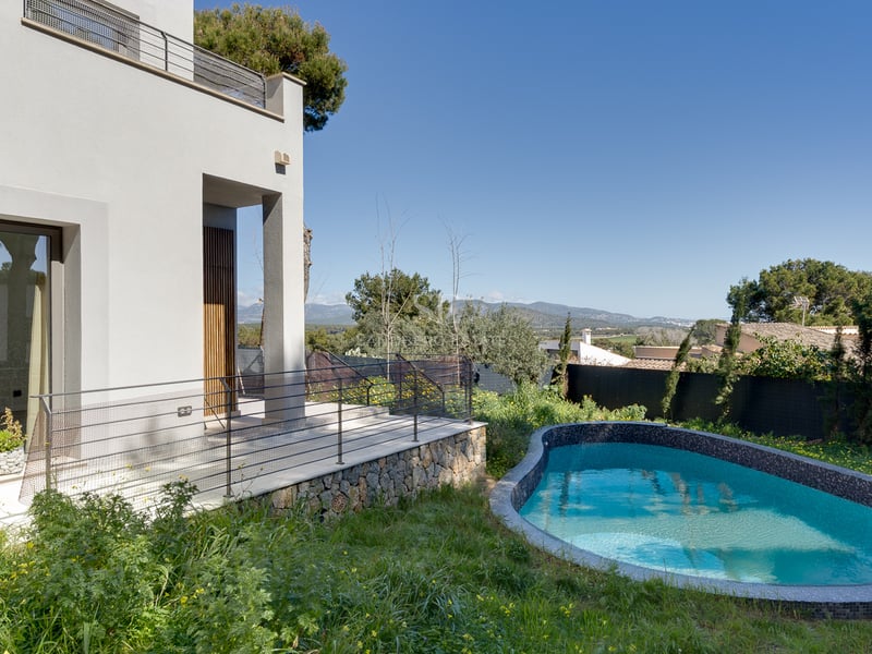 Villa blanche moderne avec piscine courbe en mosaïque bleue, base en pierre et vue sur la montagne par temps clair.