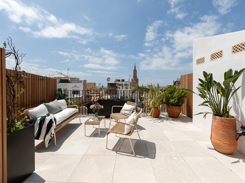 Terraza moderna en la azotea con muebles de exterior, suelo de piedra y vistas a la catedral de Palma bajo un cielo azul.
