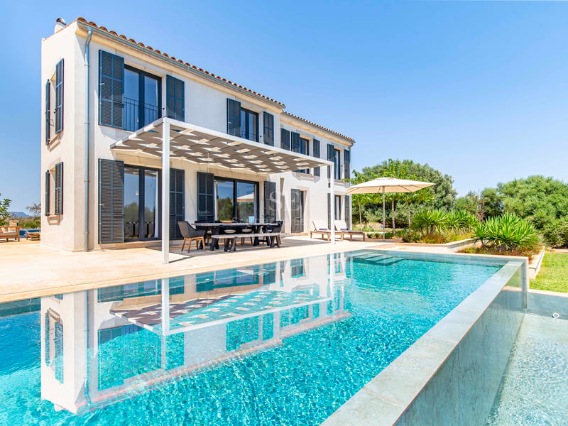 Luxury villa exterior featuring a turquoise swimming pool and a shaded dining terrace under a clear blue sky.