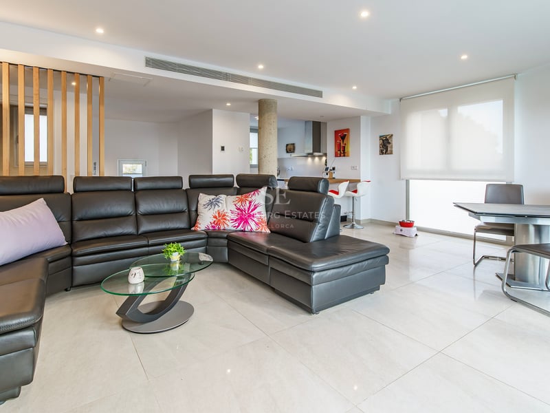 Salon spacieux avec un grand canapé en cuir noir, table basse en verre et coin repas moderne.