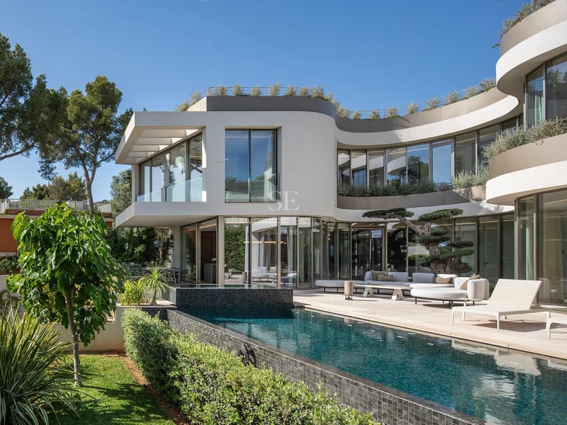 Villa blanche contemporaine aux murs courbes, piscine à débordement turquoise et salon extérieur sous un ciel bleu.