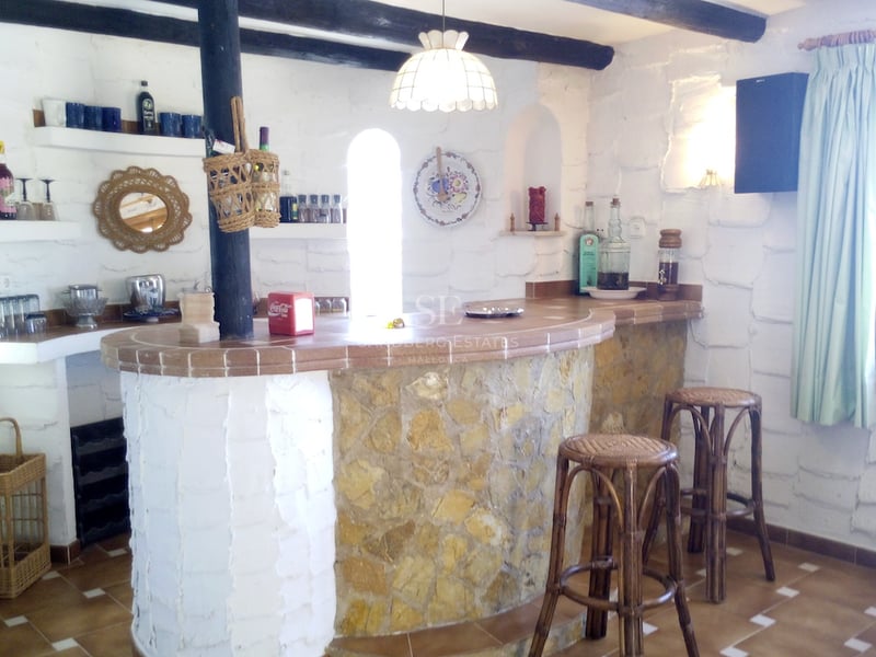 Bar intérieur incurvé avec façade en pierre, comptoir en terre cuite et poutres de plafond en bois.