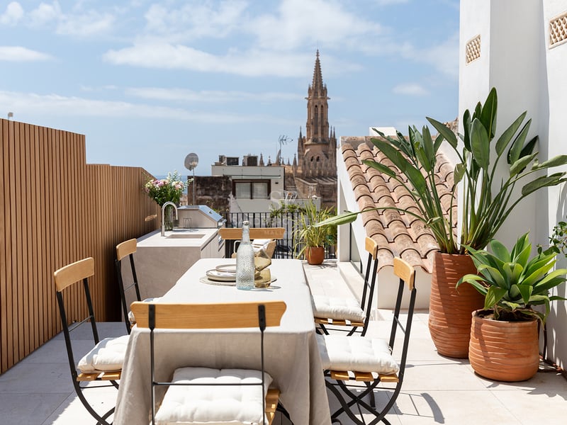 Terraza moderna en azotea con comedor exterior, cocina de verano y vistas a una catedral gótica histórica.