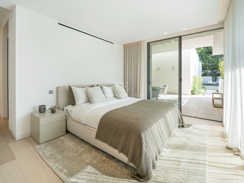 Chambre moderne avec grand lit, parquet clair et baies vitrées coulissantes ouvrant sur une terrasse privée.