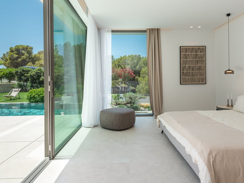 Chambre contemporaine avec baies vitrées coulissantes ouvrant sur une piscine turquoise et un jardin luxuriant.