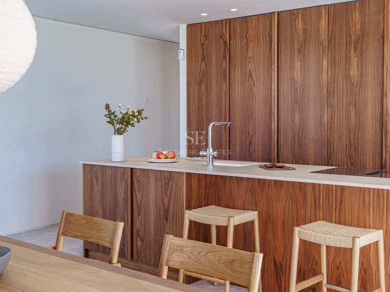 Cuisine moderne avec menuiserie en noyer, îlot avec plan de travail en pierre et tabourets en bois et osier.