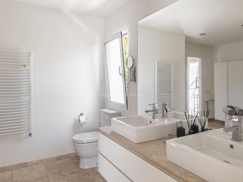 Salle de bain lumineuse avec double vasque sur plan en pierre naturelle, grand miroir et sèche-serviettes blanc.