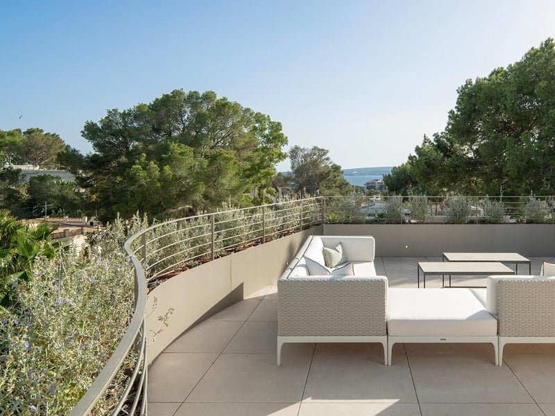 Terrasse moderne avec salon de jardin blanc, garde-corps métallique et vue sur les pins et la mer.