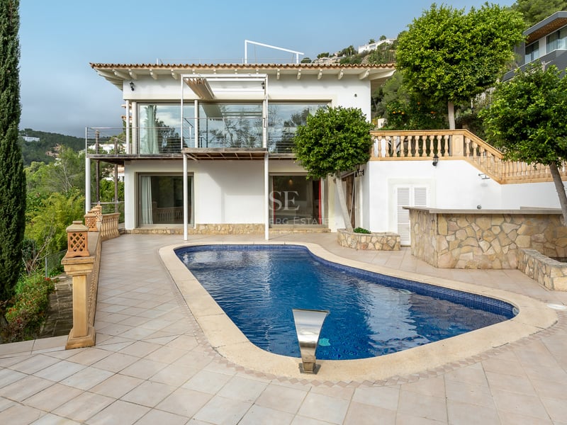 Piscine bleue sur une terrasse carrelée devant une villa blanche de style méditerranéen avec des cyprès.