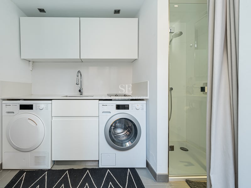 Espace buanderie blanc avec lave-linge et sèche-linge Miele à côté d'une douche vitrée.