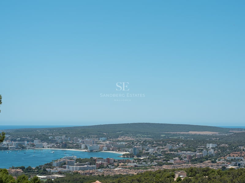 Vue panoramique surélevée d'une baie méditerranéenne bleue, d'une ville côtière et de collines verdoyantes.