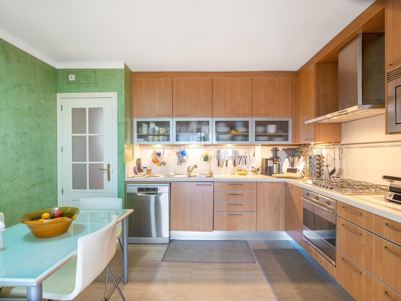 Cuisine contemporaine en bois avec appareils en inox, mur vert texturé et table de salle à manger en verre.