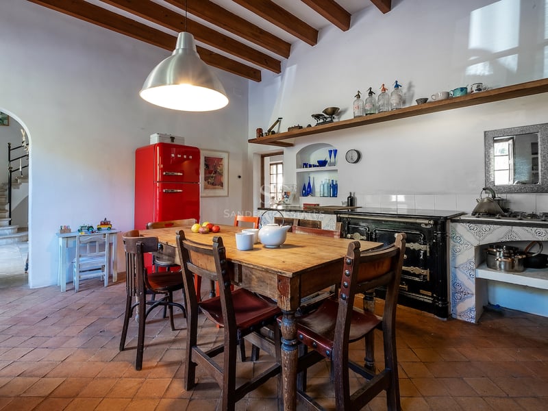 Cuisine traditionnelle avec sols en terre cuite, poutres en bois, table rustique et réfrigérateur rouge vif.