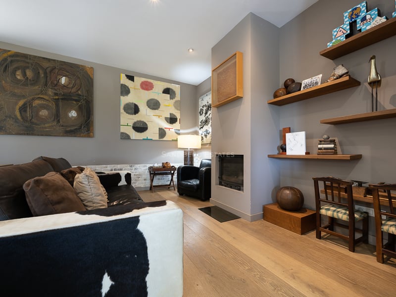 Salon moderne avec canapé en peau de vache, cheminée minimaliste, parquet en chêne et art éclectique.