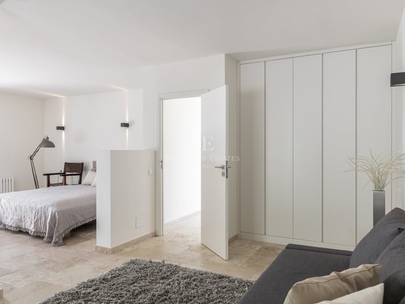 Chambre moderne avec carrelage en pierre beige, placards blancs, canapé gris et appliques murales minimalistes.