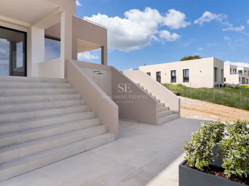 Escaliers en pierre naturelle menant à une villa moderne beige sous un ciel bleu.