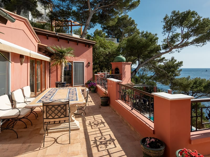 Terrasse en terre cuite avec table à manger, ferronnerie d'art et vue mer à travers les pins.