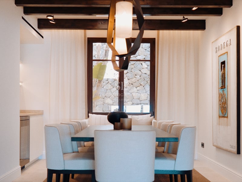 Salle à manger contemporaine avec chaises rembourrées, lustre sculptural et poutres en bois sombre au plafond.