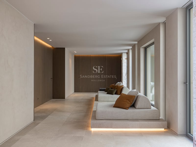 Salon minimaliste avec banquettes basses, murs en pierre naturelle et éclairage LED indirect chaleureux.