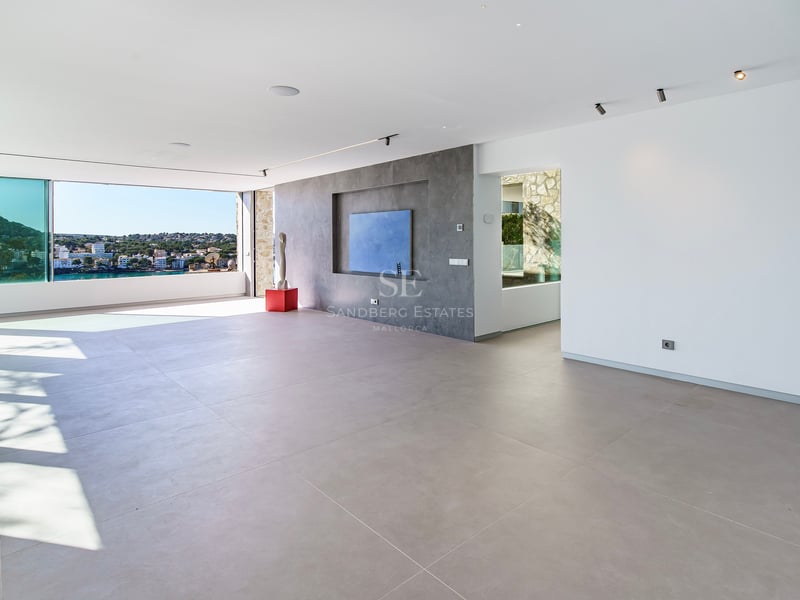 Grand salon minimaliste avec carrelage gris, murs blancs et baies vitrées offrant une vue panoramique sur la côte.