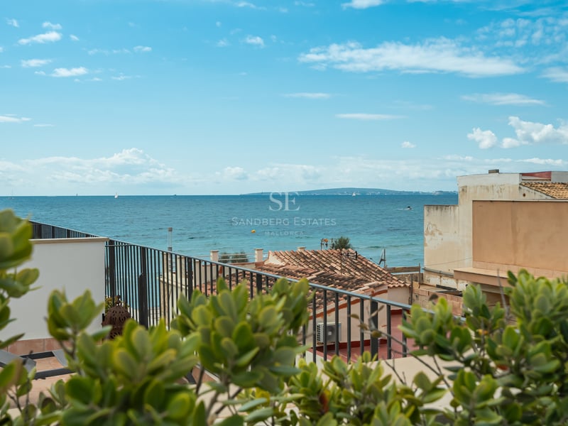 Vue sur la mer Méditerranée bleue depuis une terrasse avec une balustrade en métal noir et des toits en terre cuite.
