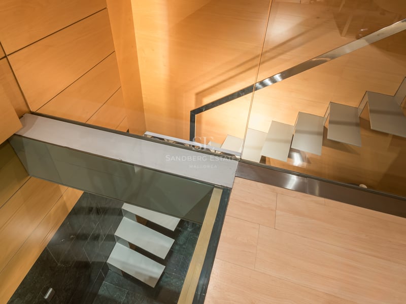 Top-down view of modern floating staircase with glass railings and warm wood wall paneling.