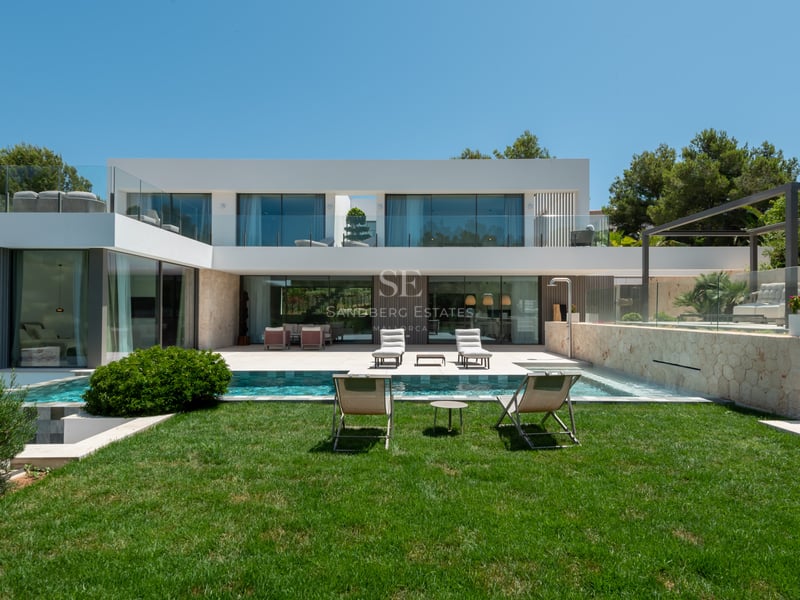 Vue arrière d'une villa contemporaine blanche sur deux niveaux avec piscine, jardin et murs en pierre naturelle.