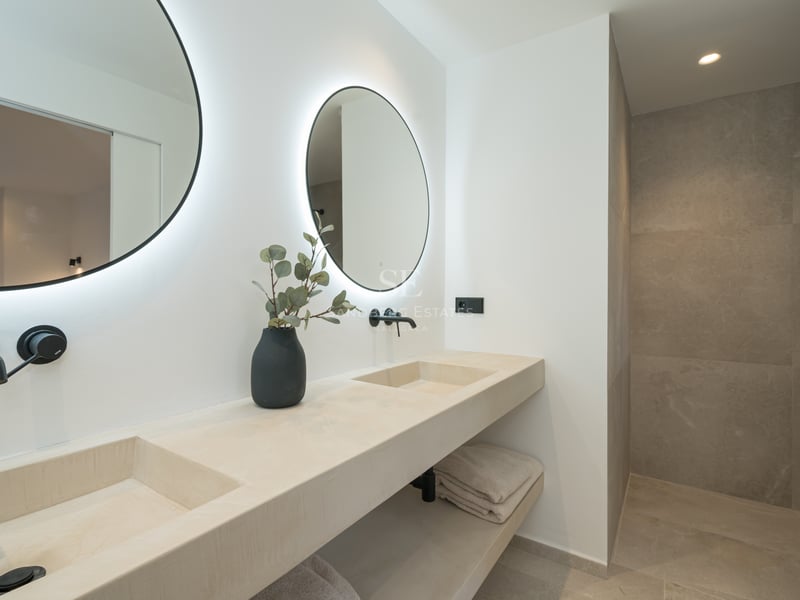 Salle de bains minimaliste avec deux miroirs ronds rétroéclairés, double vasque en pierre et robinetterie noir mat.