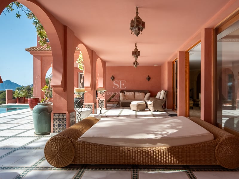 Terrasse ombragée aux murs terracotta avec arches, lits de repos en osier et lanternes artisanales.