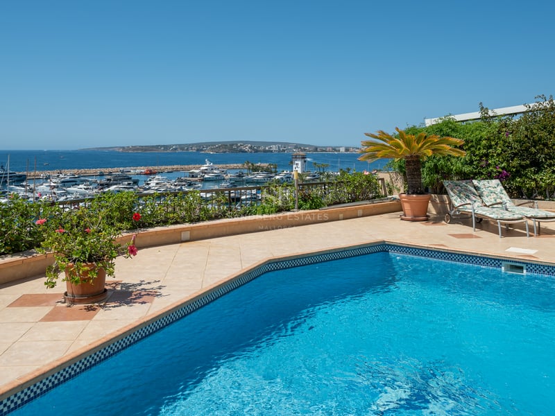 Piscine sur une terrasse en carrelage surplombant un port de plaisance de luxe et la mer Méditerranée.