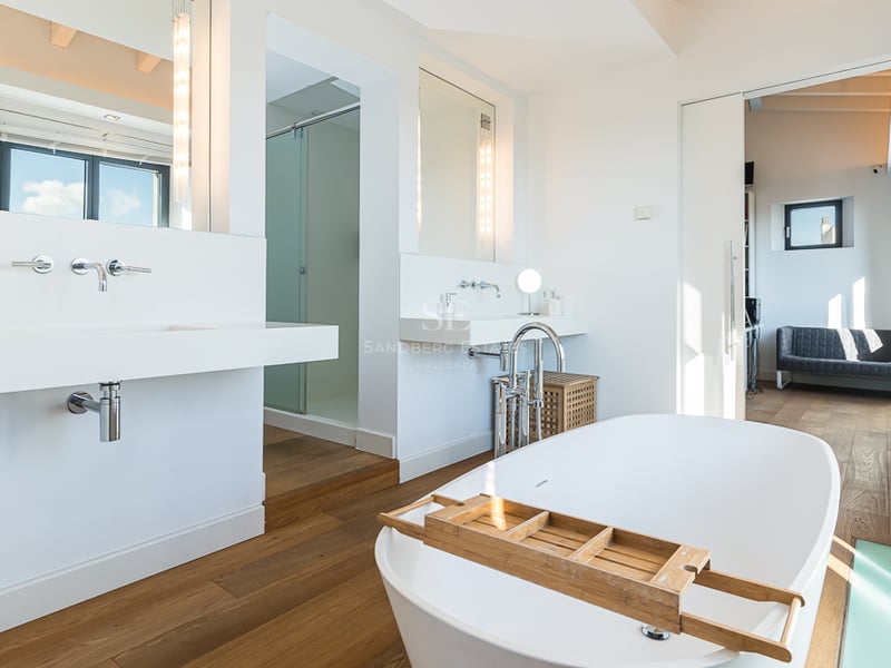 Salle de bain principale lumineuse avec baignoire îlot blanche, parquet et lavabos suspendus modernes.