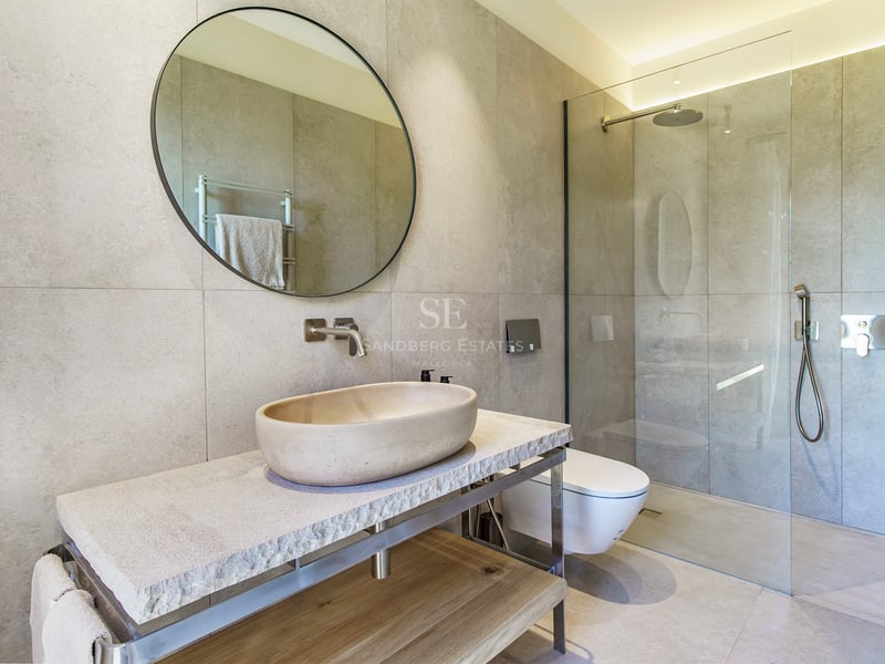 Baño contemporáneo con lavabo ovalado de piedra, espejo circular y ducha de cristal con azulejos de gran formato.