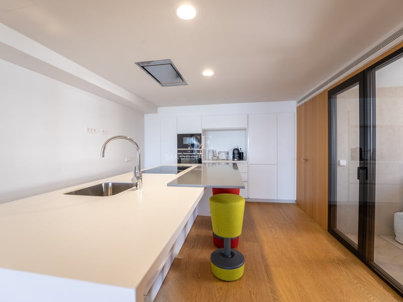 Intérieur de cuisine moderne avec un grand îlot blanc, un évier, du parquet et des appareils encastrés.
