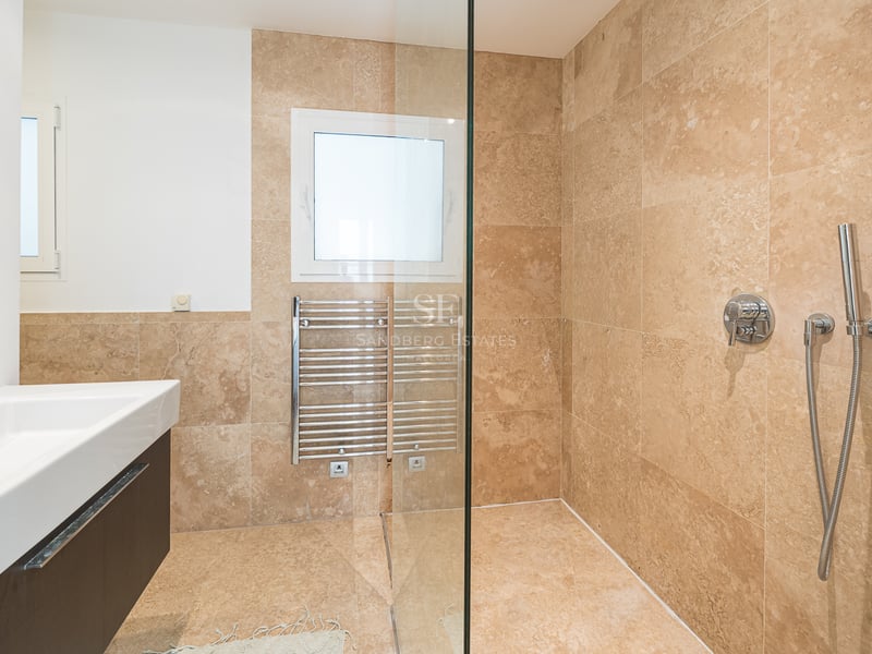 Salle de bain moderne avec carrelage en travertin beige, douche à l'italienne vitrée et sèche-serviettes.