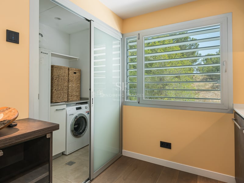 Buanderie moderne avec lave-linge dissimulé derrière une porte en verre dépoli et fenêtre à persiennes.